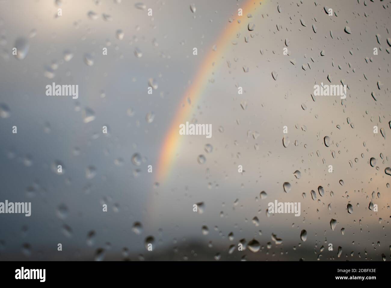 Rainbow seen thru wet window with water drops Stock Photo