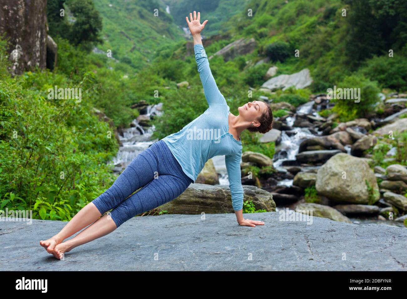 Yoga outdoors - beautiful sporty fit woman doing yoga asana Vasisthasana - side plank pose at tropical waterfall Stock Photo
