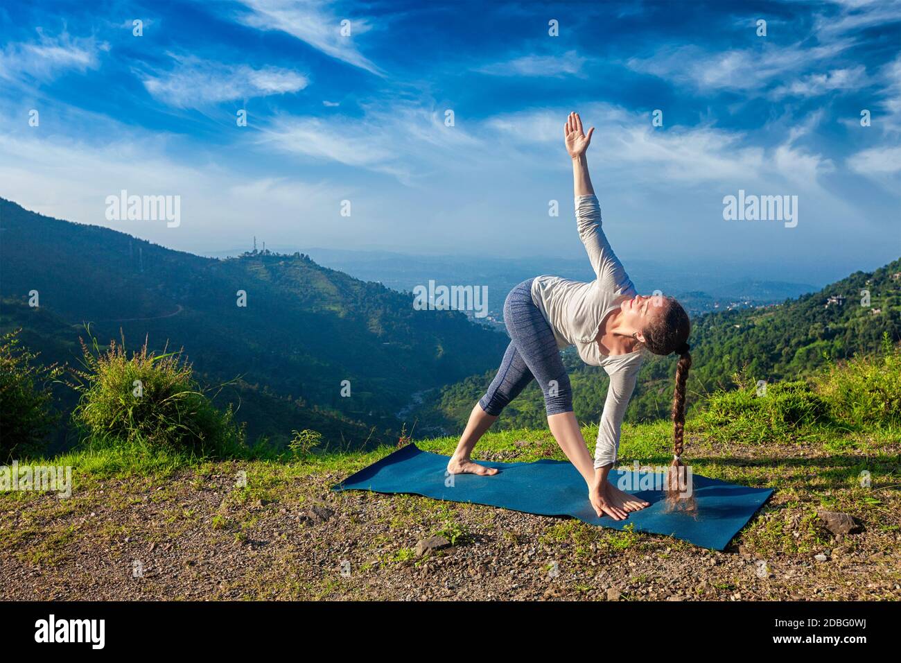 Woman doing Ashtanga Vinyasa yoga asana Parivrtta trikonasana - revolved triangle pose outdoors in mountains in the morning Stock Photo