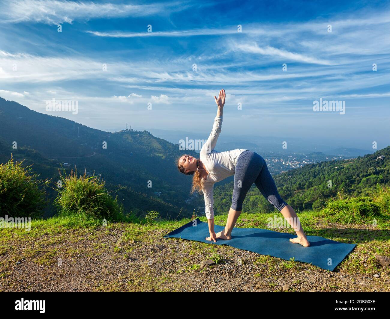 Woman doing Ashtanga Vinyasa yoga asana Parivrtta trikonasana - revolved triangle pose outdoors in mountains in the morning Stock Photo