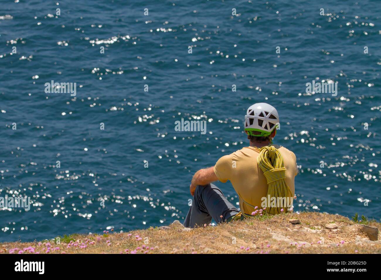 Rock climber In Helmet With Rope On Back Sitting On A Cliff Top Staring Out To Sea Contemplating The Next Climb, Durlston Swanage UK Stock Photo