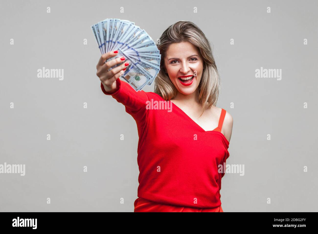 Portrait Of Excited Rich Beautiful Woman In Red Dress Standing Showing Dollar Bills To Camera
