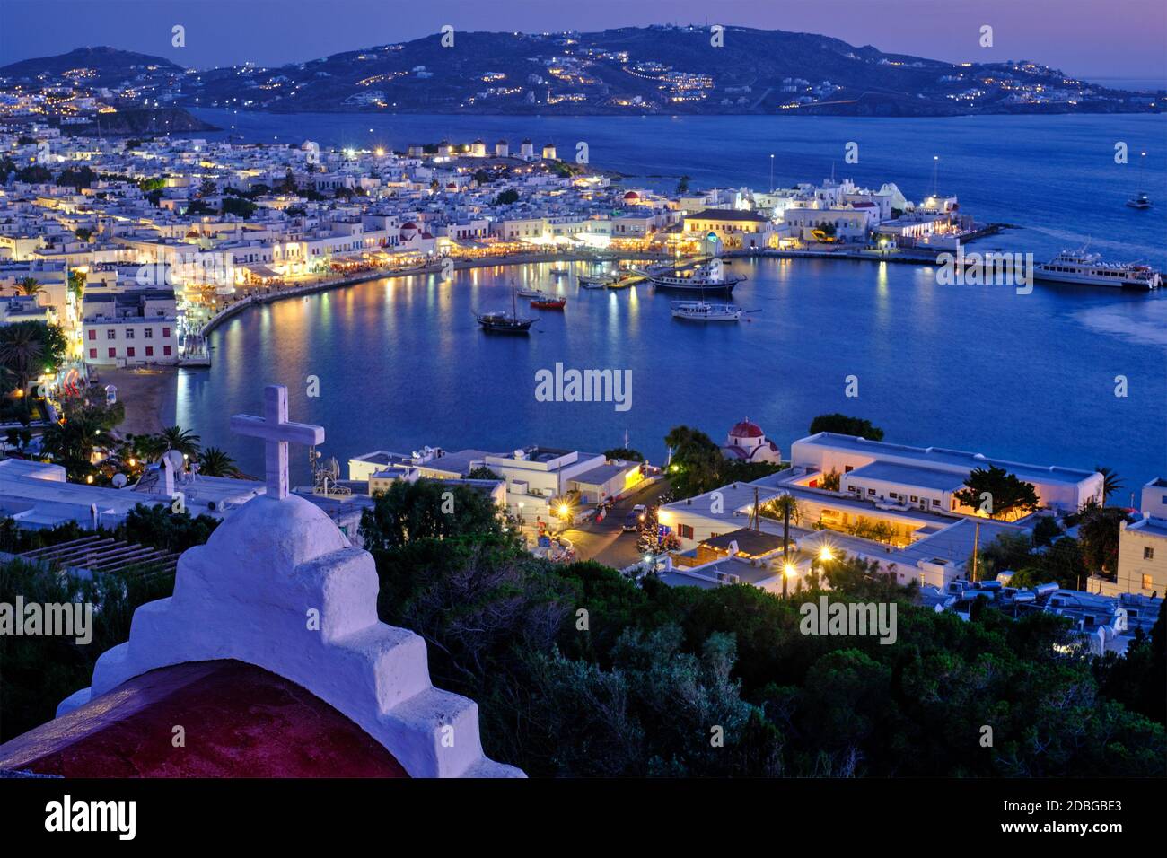 Mykonos Chora town Greek tourist holiday vacation destination with famous windmills port with boats yachts illuminated in evening blue hour with St. B Stock Photo