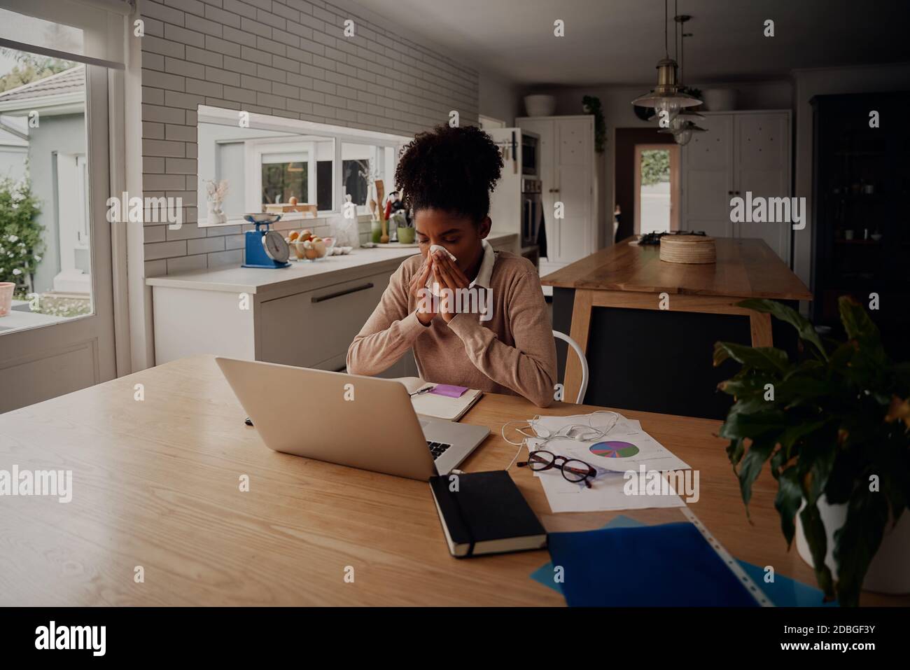 Woman sitting alone blowing nose while using laptop during work from home Stock Photo