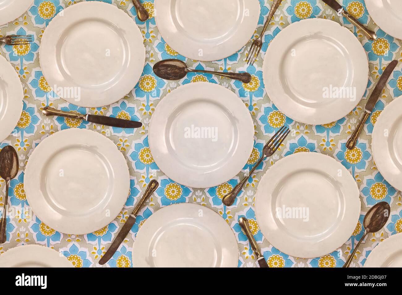 Pattern of vintage dinner plates, knives, forks and spoons on a flower cloth Stock Photo