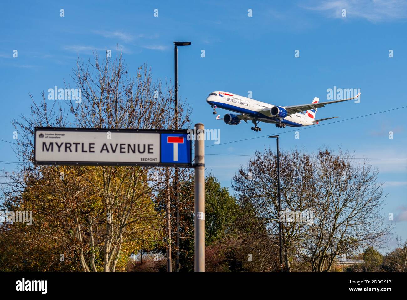 British Airways jet airliner plane on approach to land at London Heathrow Airport, UK, over residential area in Myrtle Avenue. Low flying. Street sign Stock Photo