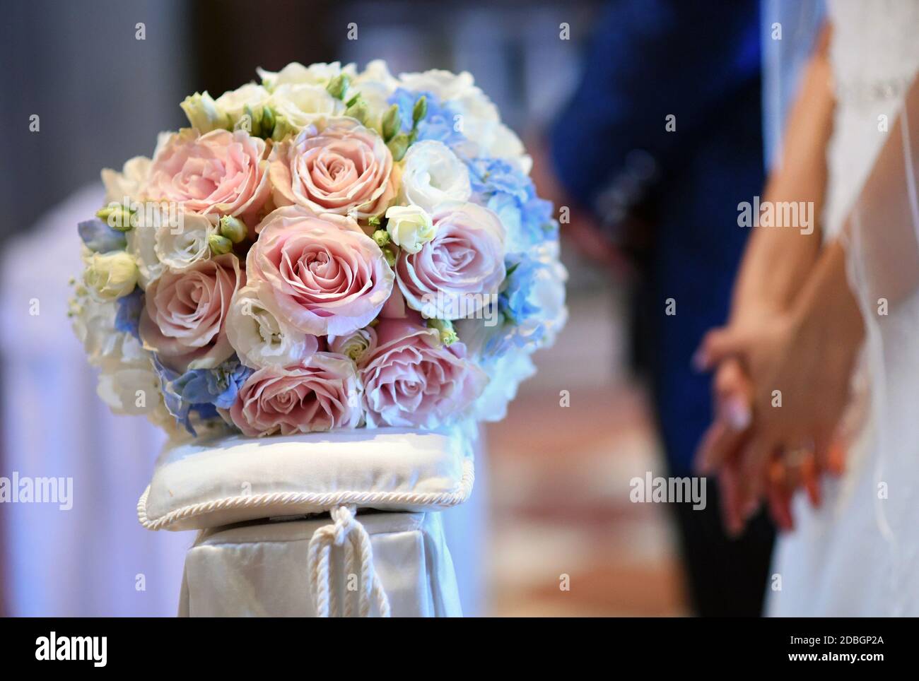 Bridal posy on a cushion with groom and bride in the background holding hands with selective focus to the flowers Stock Photo