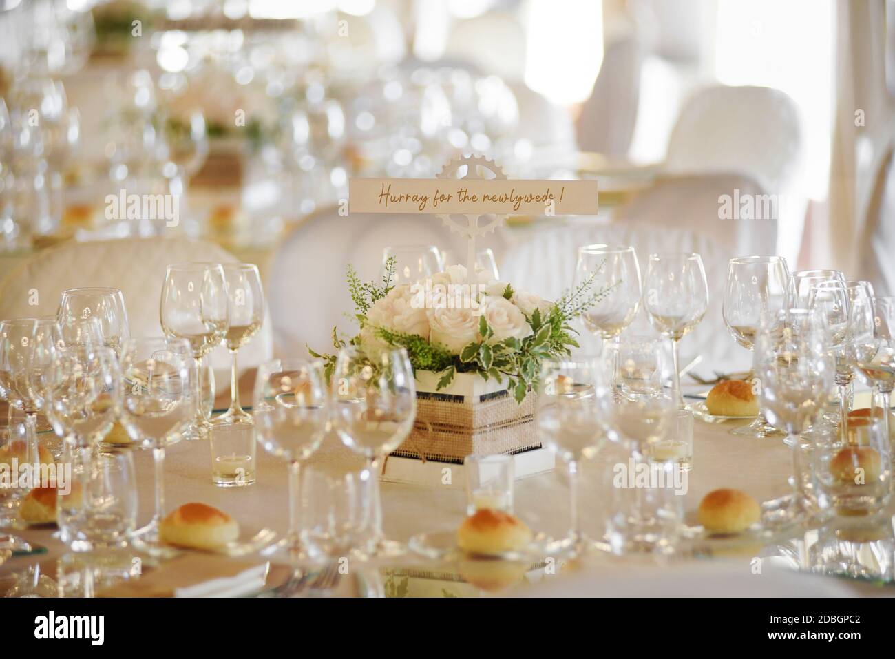 Wedding venue with formal table settings with elegant glassware and small bread rolls around a centrepiece with handwritten message Stock Photo