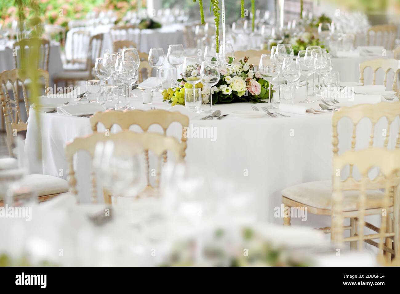 Formal table settings at a wedding venue with stylish white chairs, elegant glassware and silverware around floral centrepieces with selective focus t Stock Photo
