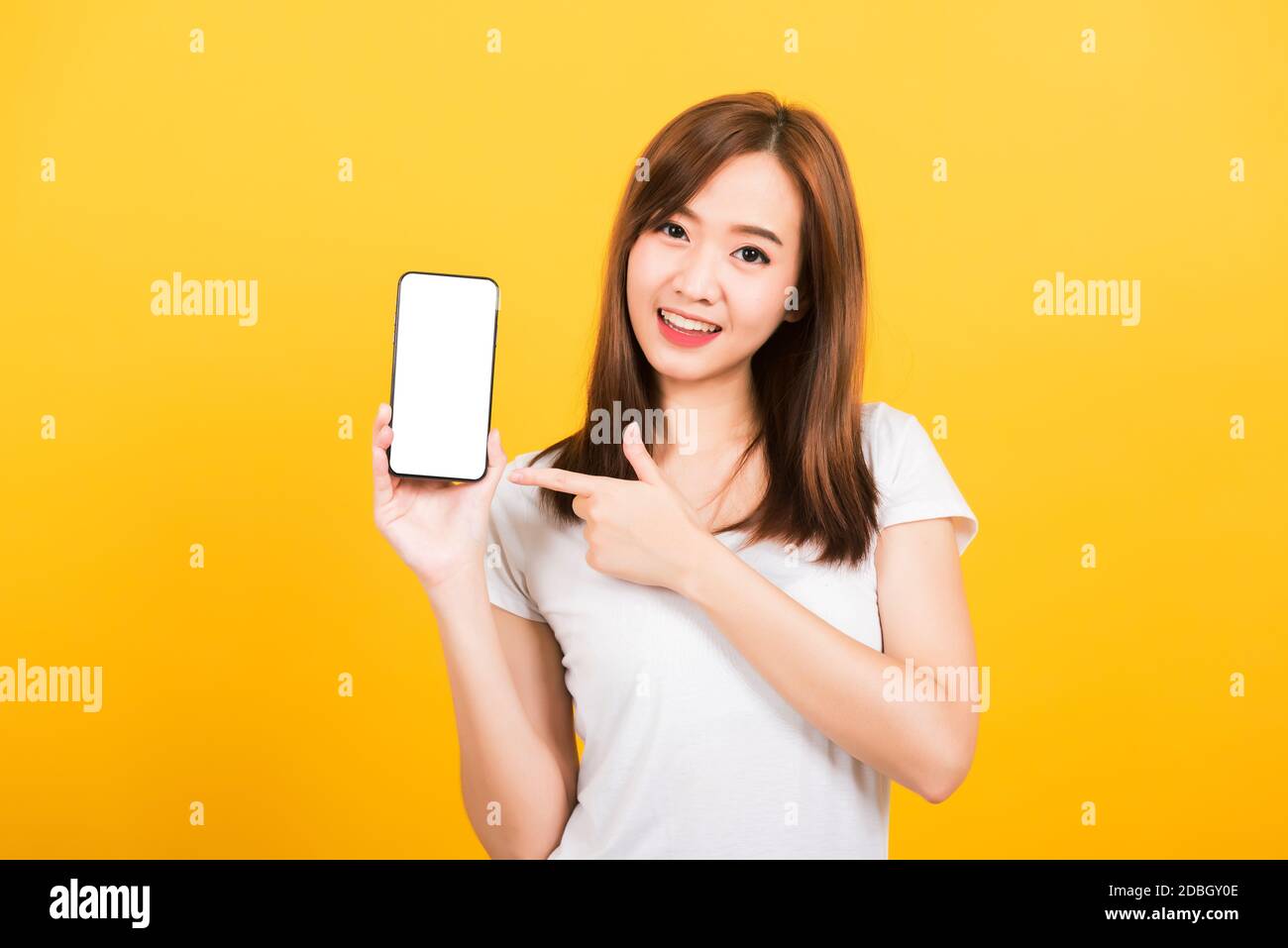Asian happy portrait beautiful cute young woman smile standing wear t-shirt making finger pointing on smartphone blank screen looking to camera isolat Stock Photo