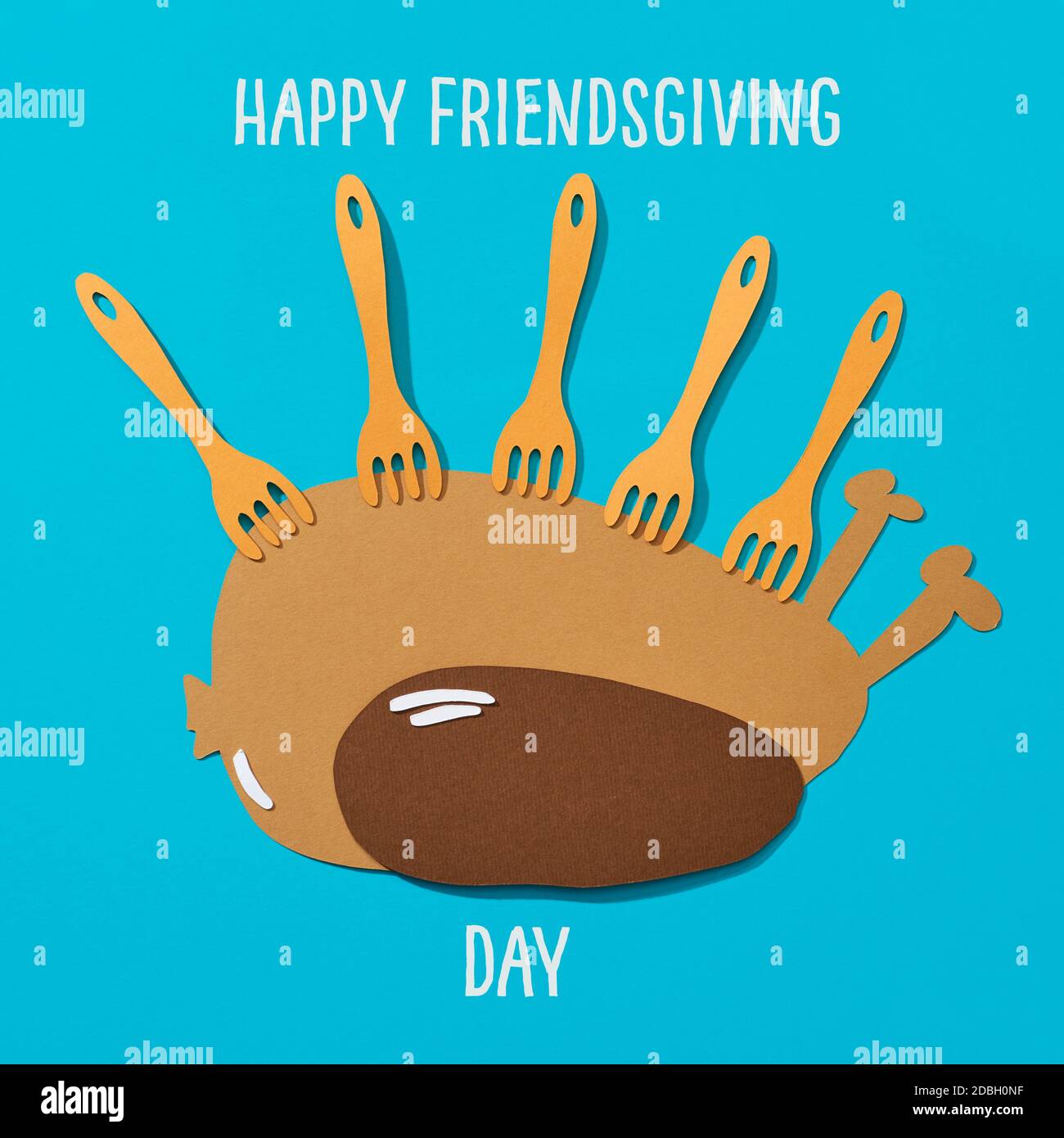 paper cutouts in the shape of a roast turkey and some forks, and the text happy friendsgiving day in white on a blue background Stock Photo