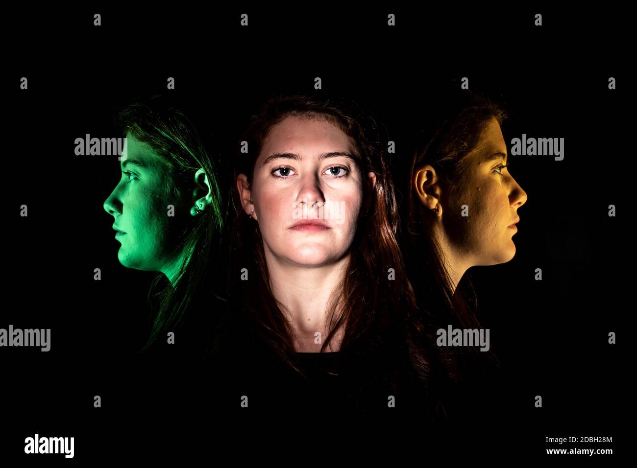 Face of a young woman frontal and multicolored in profile against a black background Stock Photo