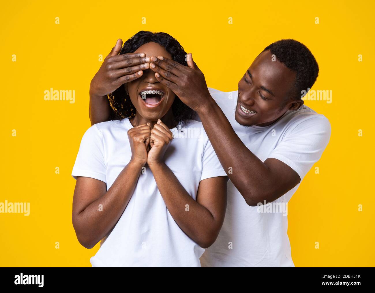 Black guy covering his girlfriend eyes, yellow studio background Stock ...