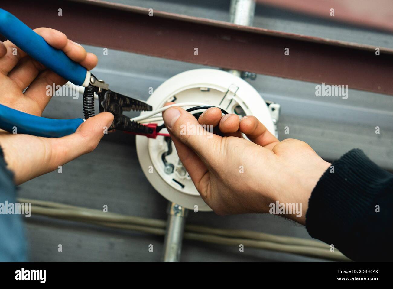 Technician's hands install fire alarm wire in metal ceiling industrial