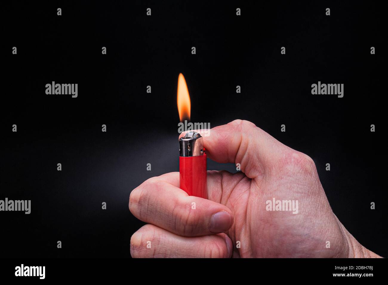 European white mans hand holds a burning red ignited plastic gas lighter with fire on an isolated black background Stock Photo