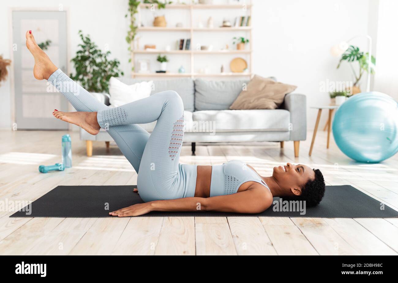 Sports training at home. Attractive young woman lying on yoga mat and cycing in air, doing abs exercise in living room Stock Photo