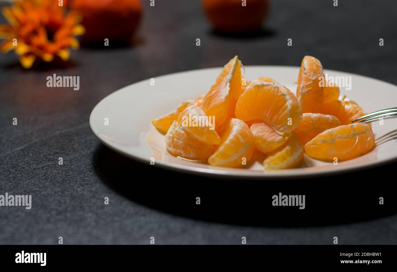 peeled oranges on a white plate on dark table Stock Photo