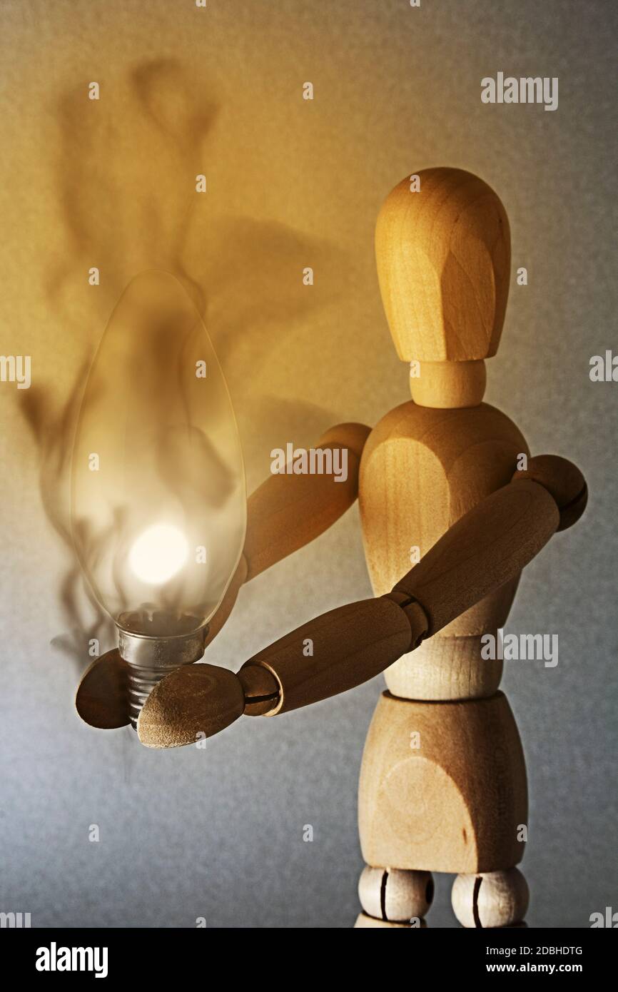 a light bulb shines in the hands of the wooden figure, the warmth of ...
