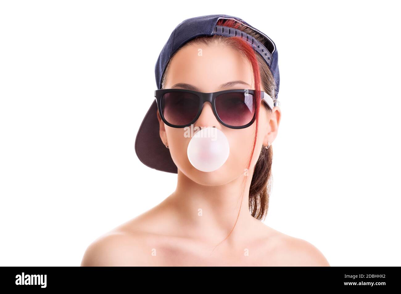 Beautiful stylish girl with backwards snapback cap and sunglasses, blowing a pink bubble with her chewing gum, isolated on white background. Stock Photo