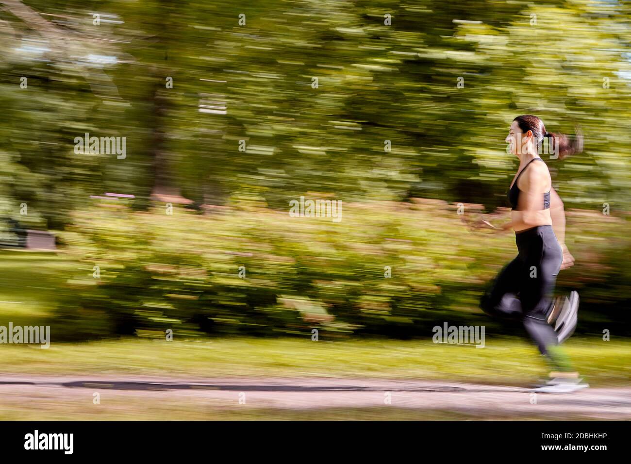 Blurred motion of woman who is running in the public park. Active white female is training in city garden at summer. Stock Photo