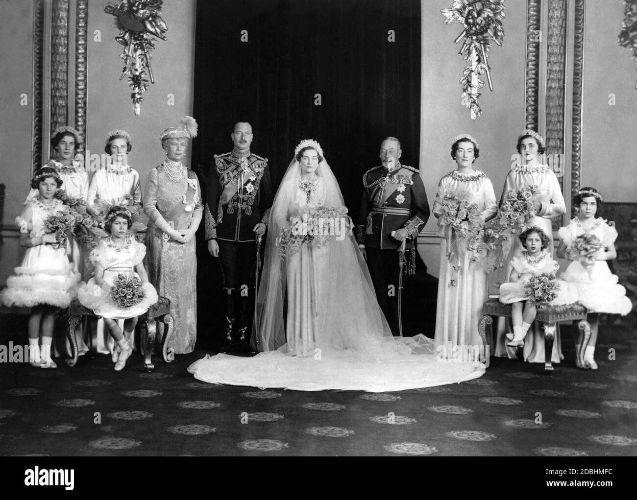 Elizabeth II at the wedding of Duke Henry of Gloucester and Lady Alice Scott (back row centre). Last row from left to right: Miss Claire Phipps, Lady Elizabeth Scott, Queen Mary, the wedding couple, King George V, Lady Angela Scott and Miss Moyra Scott. First row from left to right: Lady Mary Cambridge, Princess Elizabeth of York, Princess Margaret Rose of York and Miss Ann Hawkins. Stock Photo