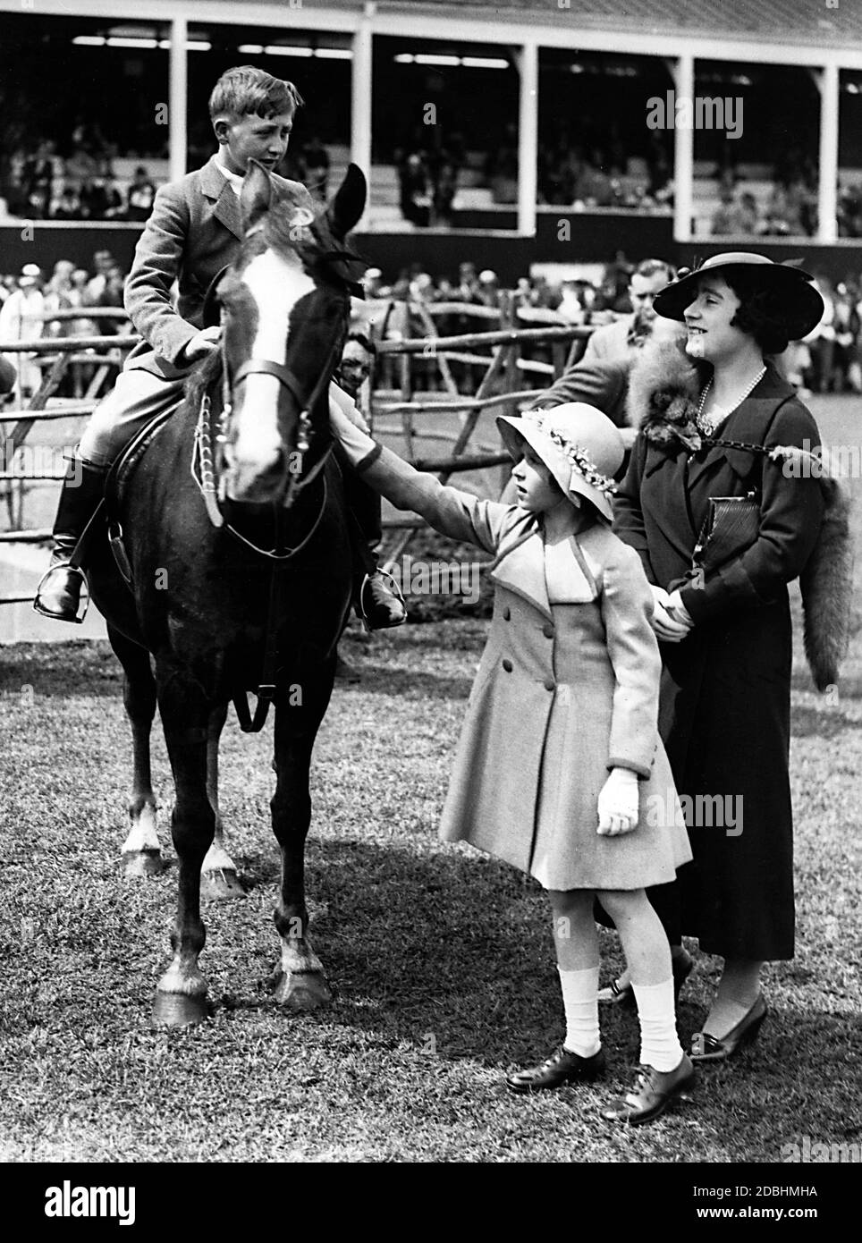 Elizabeth II with her mother Elizabeth, Duchess of York, at the Royal Horse Show in Richmond, Surrey. While Elizabeth II strokes the horse, her mother talks to Philip Gardner, the winner of the jumping class for children under 13. Stock Photo
