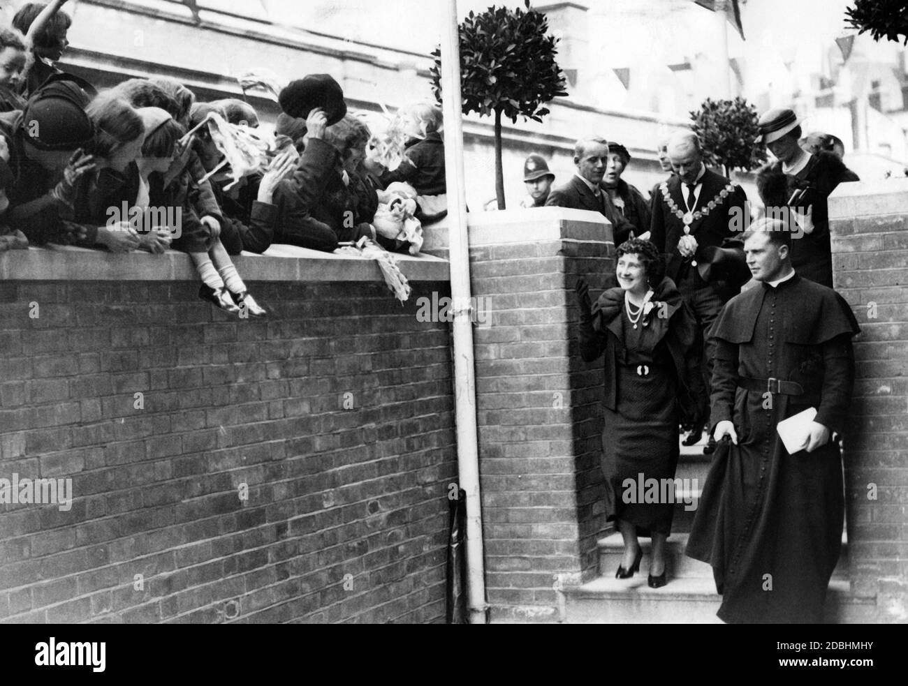 Elizabeth, Duchess of York, at the inauguration of Basil Jellicoe Hall and a new apartment block in Drummnond Crescent, Somers Town in London. The Social and Occupational Centre was founded as a memorial to the young, deceased priest Basil Jellicoe, who transformed a London slum into a garden city in 1935. The Duchess is greeted by the residents and her children with smiles and waves. Stock Photo