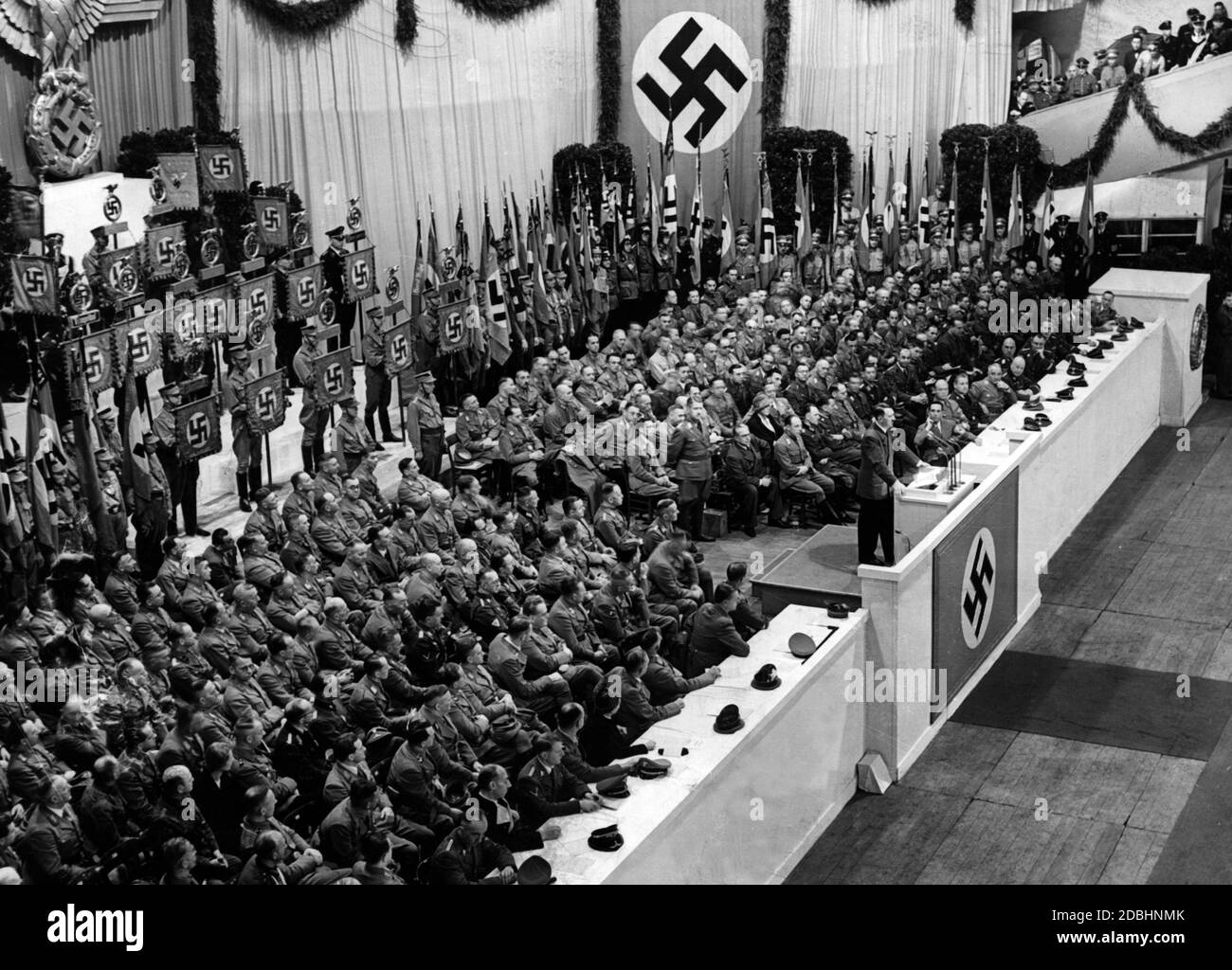 Adolf Hitler during a speech on the occasion of the upcoming fundraising for the Kriegswinterhilfswerk in the winter of 41/42. Since the beginning of the war, Hitler no longer wears a party uniform, but a field-gray jacket. On the picture are all kinds of party members of the NSDAP. To Hitler's right, Julius Schaub, Joseph Goebbels, Robert Ley, Fritz Todt, Martin Bormann, Reinhard Heydrich and Albert Speer are clearly recognizable. On Hitler's left, with their backs to the photographer, are probably Rudolf Hess, Heinrich Himmler, and Joachim von Ribbentropp. The lady with the wreath of hair Stock Photo