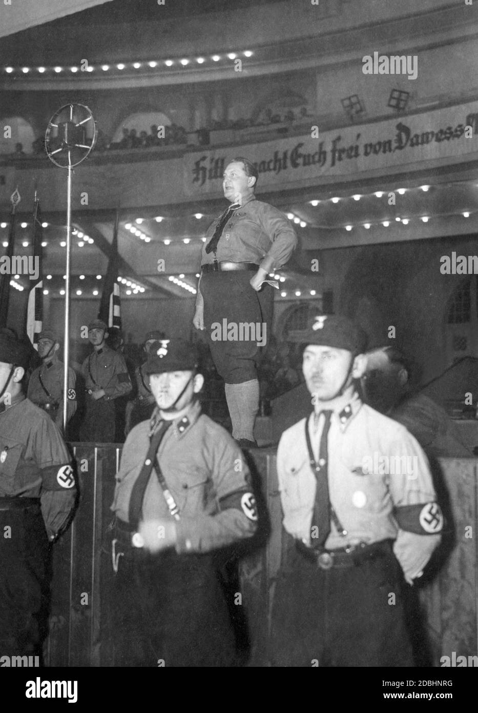 'Hermann Goering in party uniform during a speech in front of members of the NSDAP at the Sportpalast Berlin. The banner in the background reads: ''Hitler frees you from the Dawes slavery. The Dawes Plan was supposed to clarify the issue of reparations.  In the foreground are SS men. ' Stock Photo