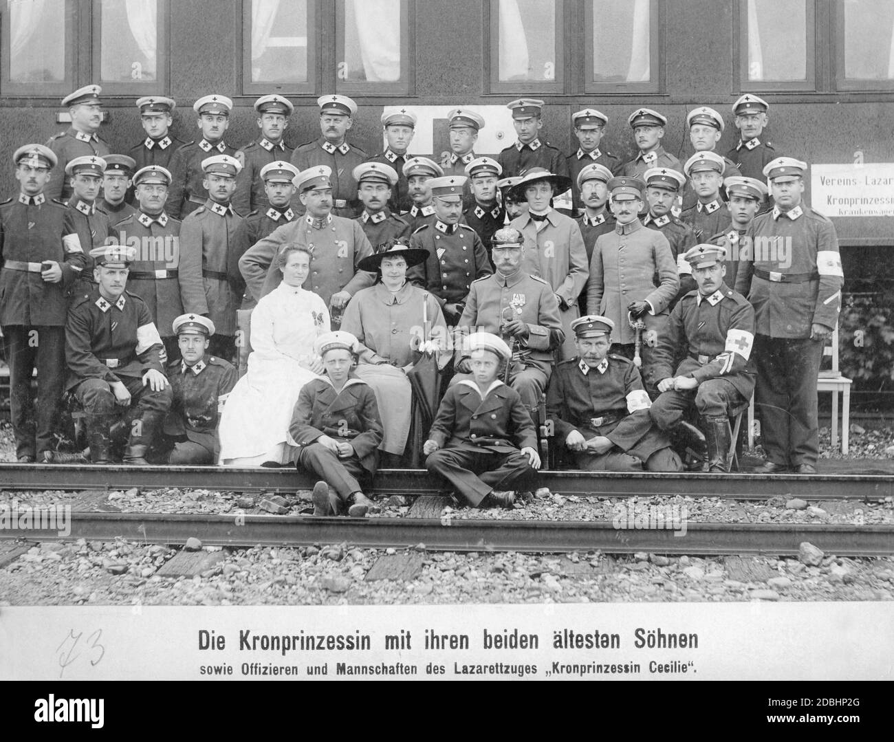 'Crown Princess Cecilie of Mecklenburg (centre of the picture, seated and wearing a women's hat) with her two eldest sons Wilhelm (left) and Louis Ferdinand of Prussia (right), who are sitting in front of her on the tracks. They are posing together with officers and teams of paramedics in front of the ambulance no. 25 of the association hospital train ''Kronprinzessin Cecilie''. This train was operated by Walter von Oettingen for the Red Cross. He is on the left behind Cecilie. In front of him is probably his wife, Elisabeth von Oettingen. The picture was taken in 1916.' Stock Photo