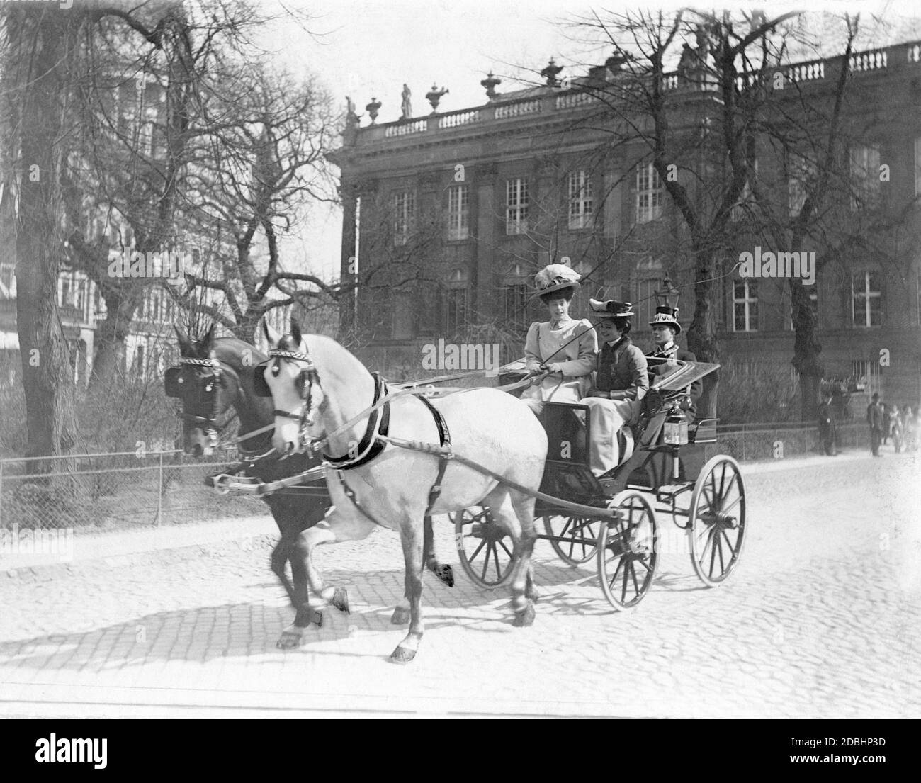 Crown Princess Cecilie of Mecklenburg sits together with a girl in a carriage and rides through Potsdam. A coachman is sitting behind them. In the background on the left, the St. Nicholas Church, on the right a part of the Potsdam City Palace. The photo was taken by the court photographer Ernst Eichgruen in 1907. Stock Photo