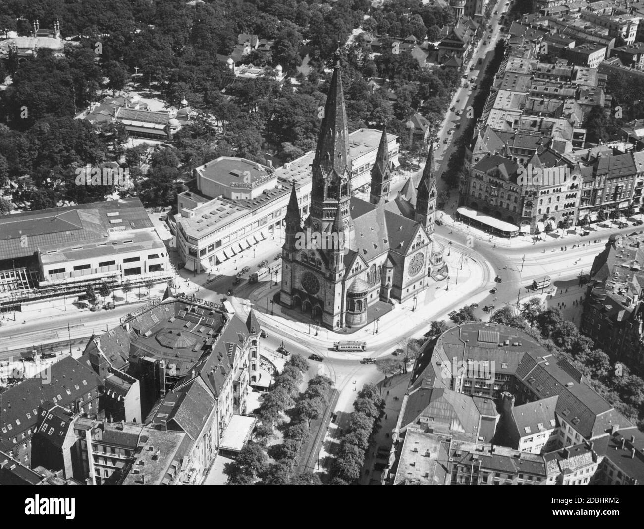 The photo shows the Kaiser Wilhelm Memorial Church at Auguste-Viktoria-Platz (today: Breitscheidplatz) in Berlin in 1938, with Budapester Strasse, Tauentzienstrasse, Rankestrasse, Kurfuerstendamm and Hardenbergstrasse leading towards the square (clockwise from above). The square is lined by the buildings: Zweites Romanisches Haus (top right), Romanisches Haus (bottom left), Ufa-Palast am Zoo (left), Capitol am Zoo (right next to it) and part of the Zoological Garden (top left). Stock Photo