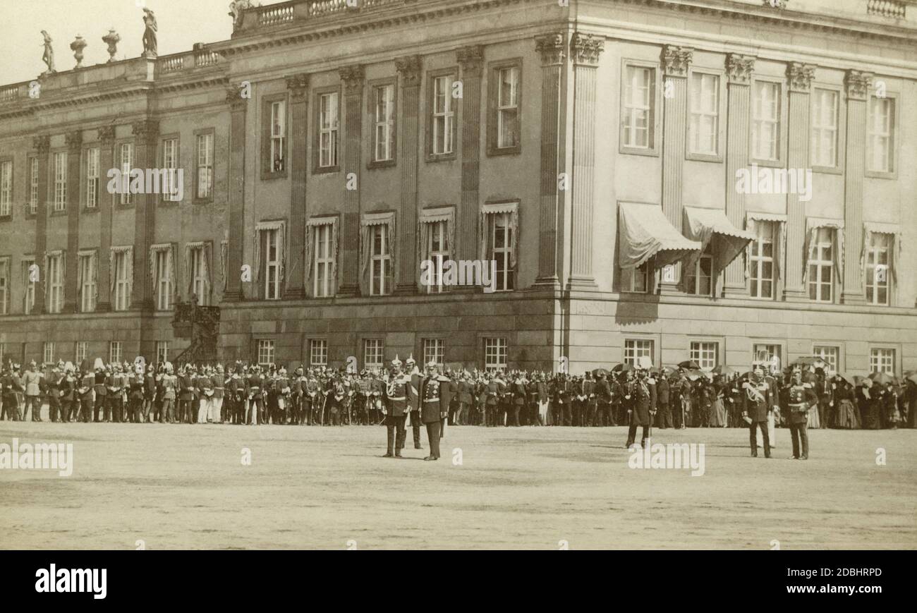 Emperor Wilhelm II (centre, left) at a public event. In the background are officers, generals, military men and ladies (right, with parasols) in front of a building in Berlin. The photo was taken around 1910. Stock Photo