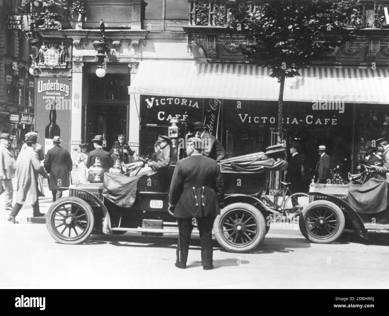 'A car stops in front of the Victoria-Cafe in the boulevard Unter den Linden, corner of Friedrichstrasse in Berlin and a passenger gets off. At the corner hangs an advertising poster for ''Underberg-Boonekamp SEMPER IDEM'' and above it a sign for ''Patentbuero Lenck''. The picture was taken around 1920.' Stock Photo