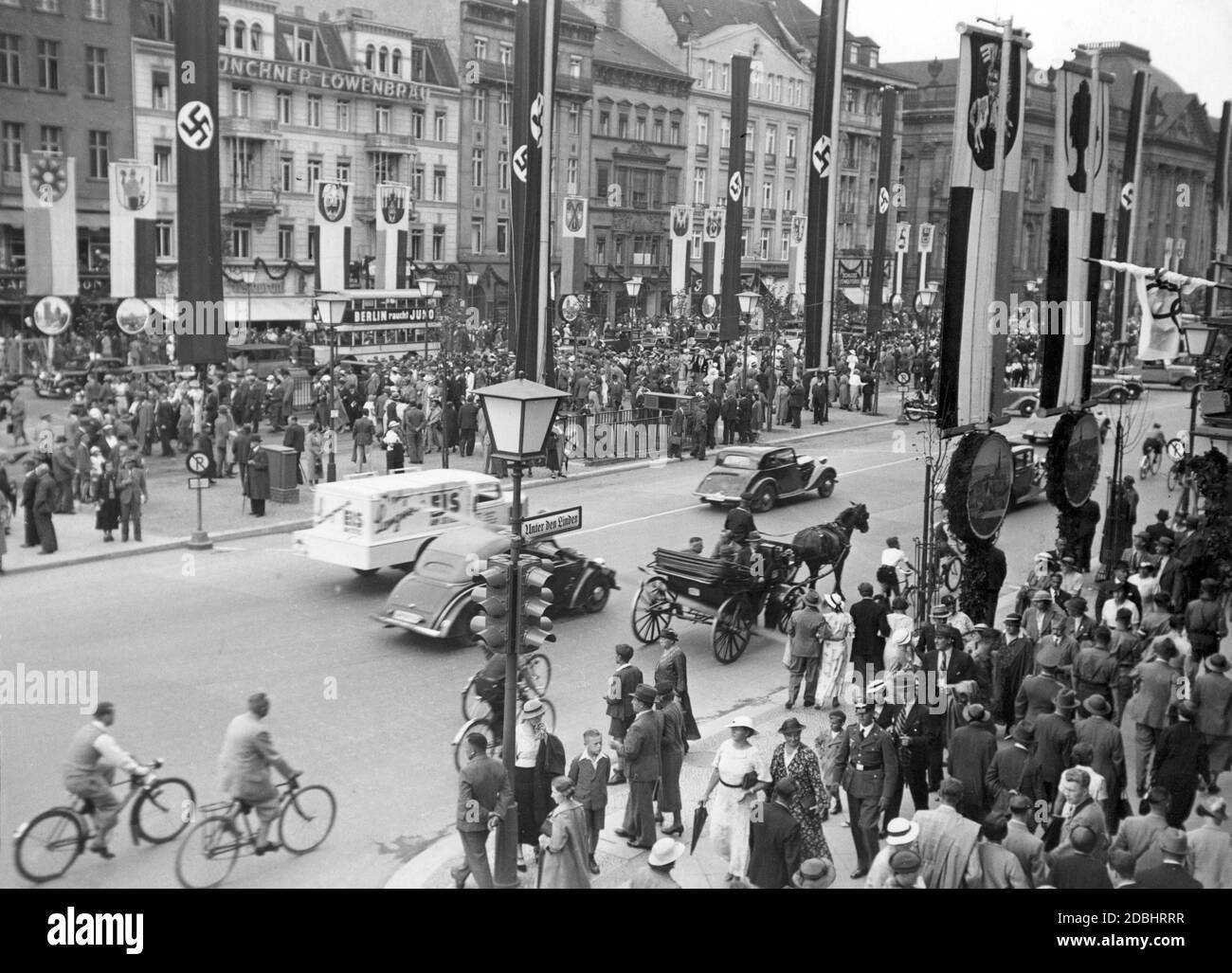 'The photograph shows the street Unter den Linden in Berlin at the level of Friedrichstrasse around the time of the 1936 Summer Olympics. Passers-by crowd on the sidewalks, in the background there is a double-decker bus with the advertising slogan ''Berlin smokes Juno'' in front of the Loewenbraeu in Munich. In the street hang swastika flags and flags with different coats of arms (presumably city arms).' Stock Photo