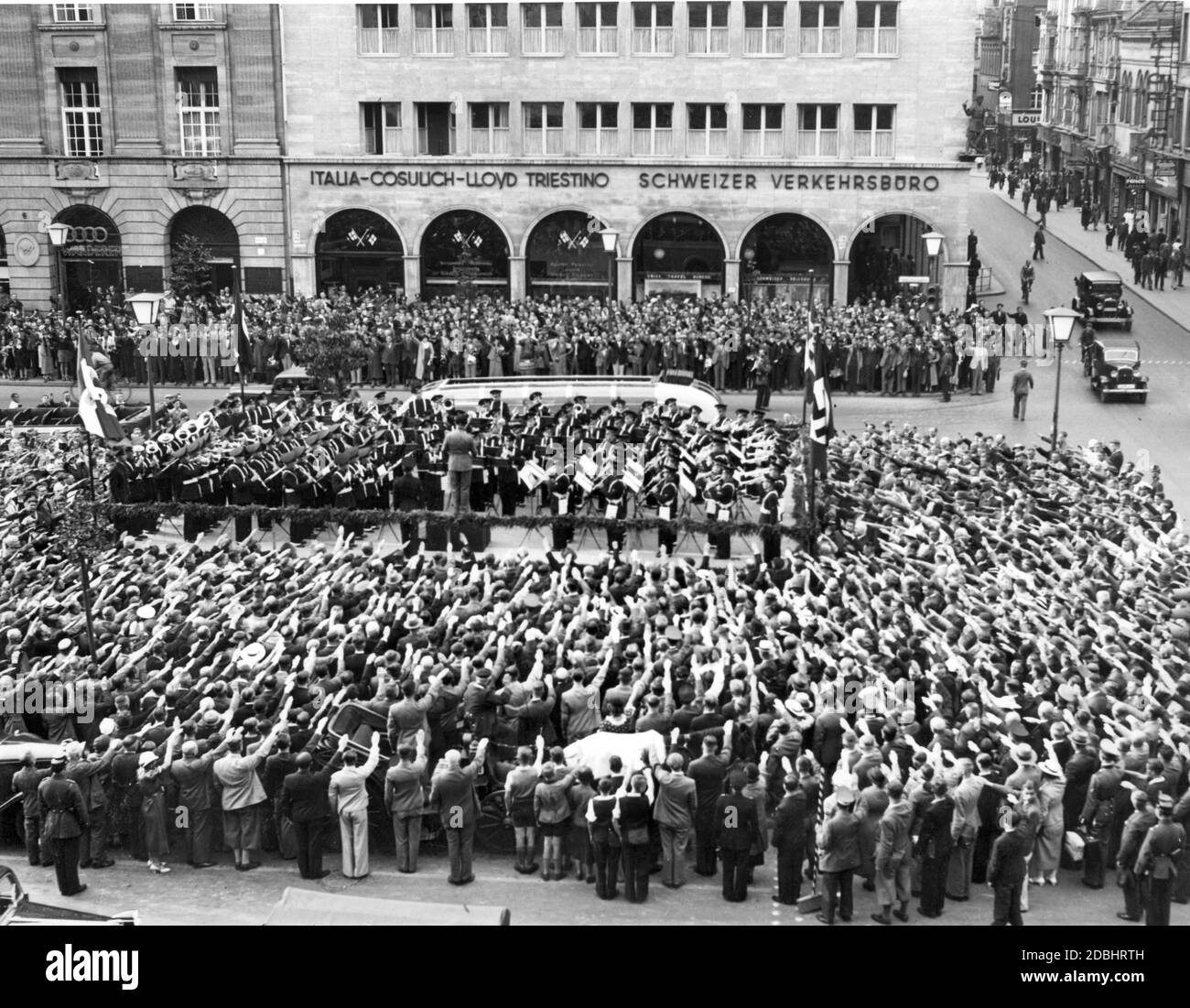 The Academia Musica of the Opera Nazionale Balilla (youth organization of the Italian fascists) plays a concert at the Kranzler-Ecke ( boulevard Unter den Linden, corner Friedrichstrasse) in Berlin in 1937. The crowd performs the Nazi salute. They stand in front of the Haus der Schweiz. On the left side there is a car dealer who sells the brands of Auto Union. Stock Photo