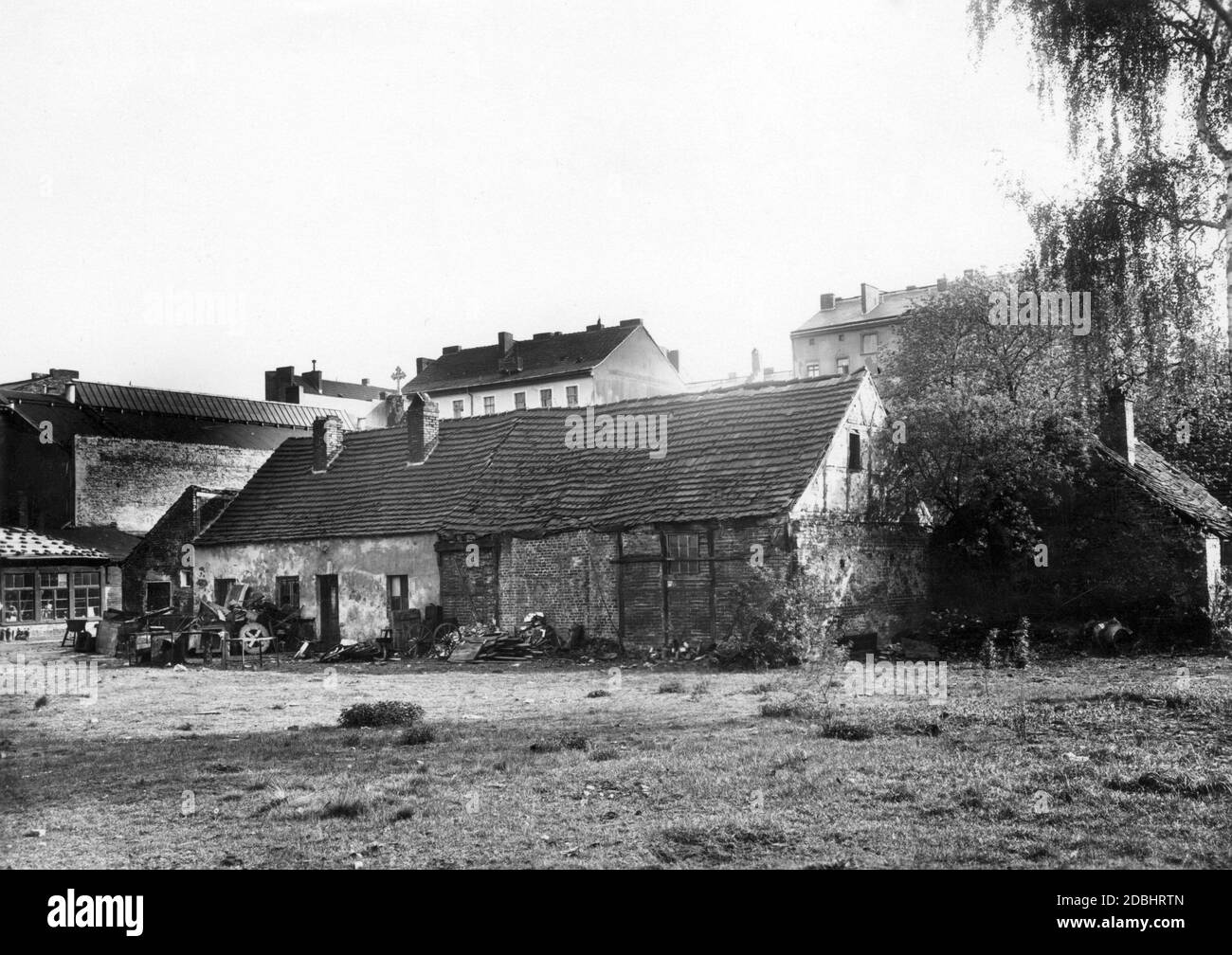 The 1932 photograph shows a decaying, abandoned old farmhouse in Berlin at Muellerstrasse 16, behind which the more modern houses and tenements of the growing city already rise up. Stock Photo