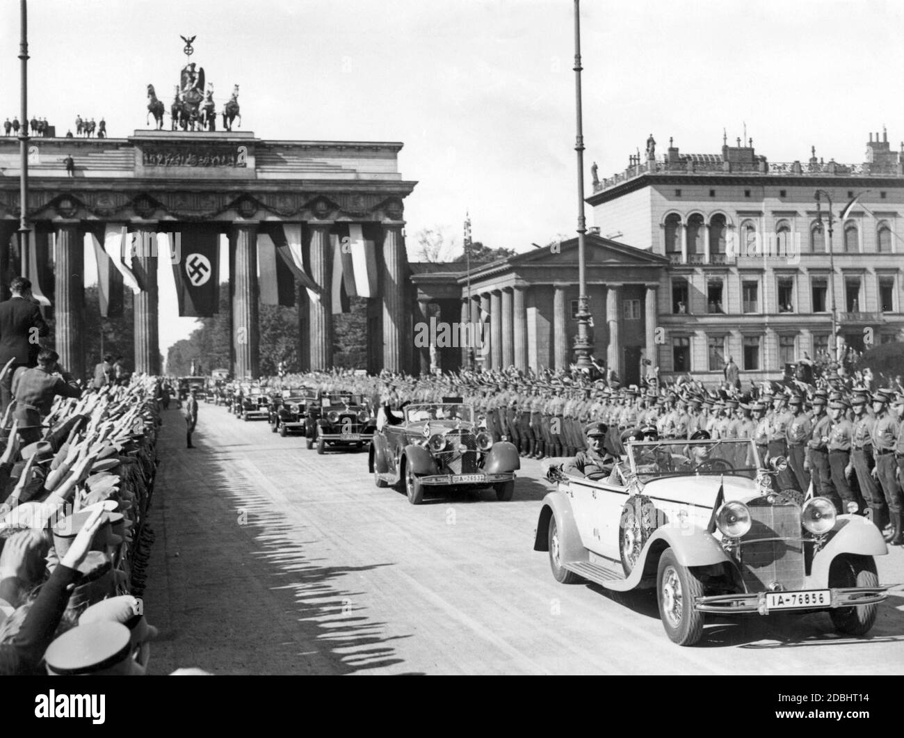 On September 15, 1933, the Prussian State Council was refounded as a purely advisory body of the National Socialists and met for its first session at the Humboldt University in Berlin. The photograph shows the entry of the Prussian state councillors through the Brandenburg Gate hung with swastika flag, cheered by a crowd of people showing the Hitler salute. In the first car, a Mercedes-Benz W10 (type Mannheim 370) with Berlin license plates, sits the Prussian Minister President Hermann Goering (2nd row left) and SA Chief of Staff Ernst Roehm (right). Behind them is a Mercedes-Benz W22 (type Stock Photo