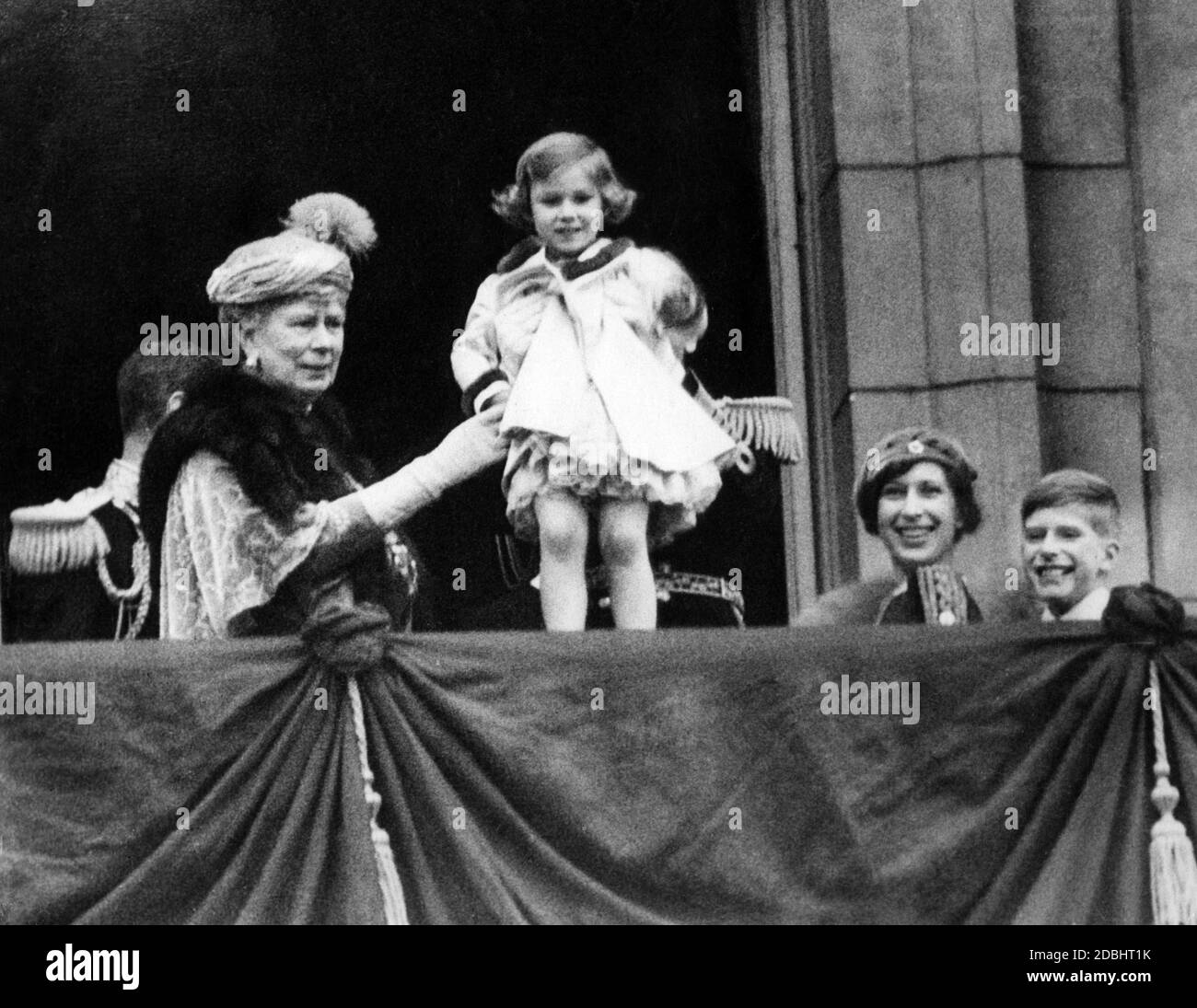 After the wedding of the Duke and Dutchess of Kent, King George V. holds up the baby Princess Margaret Rose on the balcony of Buckingham Palace. To her left stands Queen Mary. Stock Photo