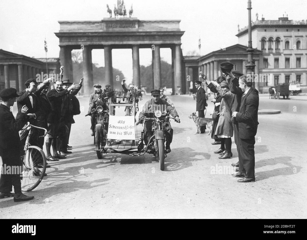 'On a Tuesday in 1928, Alfred Vollmann from Neukoelln set off on a trip around the world from the Brandenburg Gate in Berlin. The scissors grinder wanted to complete this journey with his motorcycle and grinding stone. On the motorcycle hangs a poster with the inscription ''Around the world as a scissors grinder''. On the photo he is saying goodbye.' Stock Photo