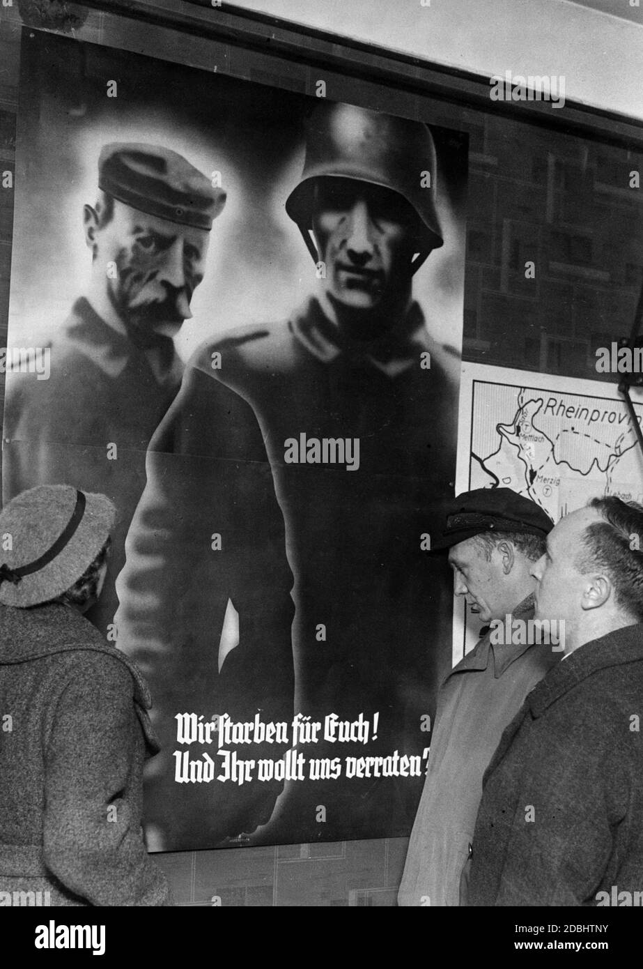 "Passers-by look at an election poster promoting the referendum in the Saar region on the annexation to the German Reich. It shows two soldiers and the inscription: 'We died for you? ""And you want to betray us?"". On the right is a map of the Saar region with the Rhine province above it." Stock Photo