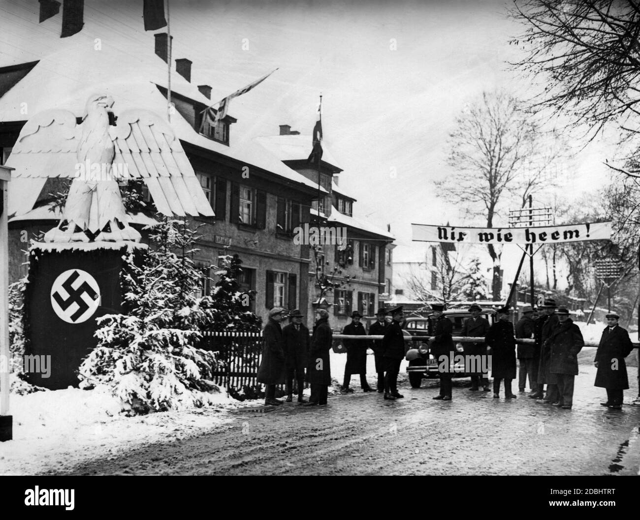 'Officials and passers-by talk at the border of Saarland. On the left, the Reichsadler (imperial eagle) standing above a swastika. On the right there is a banner stretched across the street with the writing ''Nix wie heem!''' Stock Photo