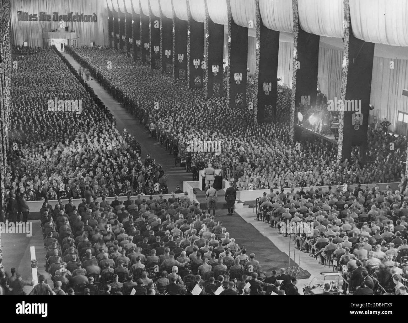 'Julius Streicher, Gauleiter of Franconia, gives a speech from the lectern at the opening ceremony of the Nazi Party Congress in Nuremberg in the festively decorated Luitpoldhalle on the Nazi Party Congress grounds. In the foreground is a music orchestra, on the right between two columns the drums. On the opposite wall is the inscription ''All for Germany''.' Stock Photo