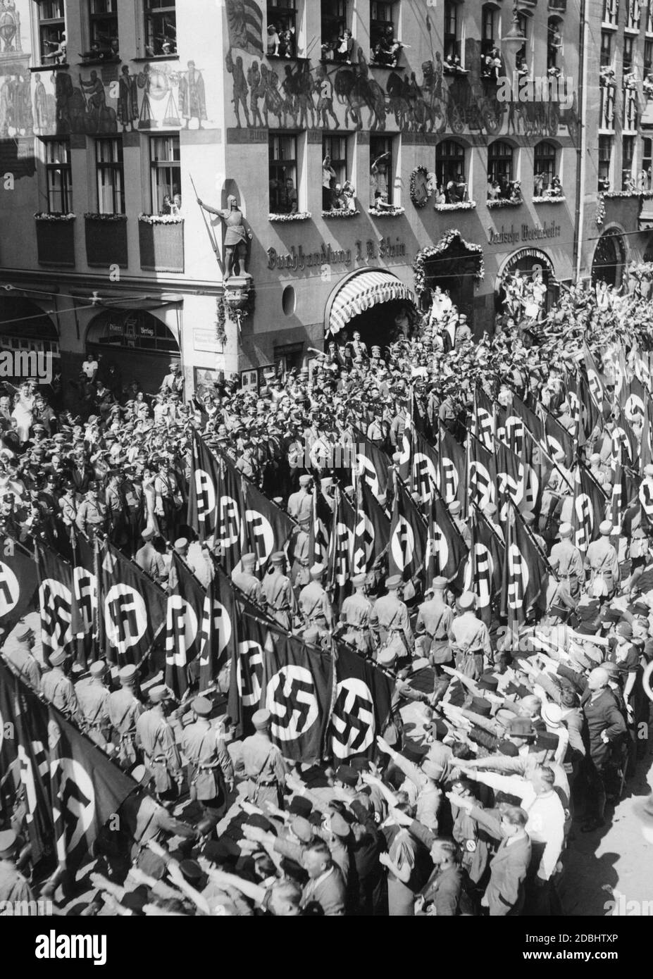 'View of the march past of the SA with swastika flags on the so-called Adolf-Hitler-Platz during the Nazi Party Congress in Nuremberg, as they are greeted by the crowd. In the background the bookstore ''Buchhandlung J.A. Stein - Deutsche Wertarbeit'', on the facade of which are paintings and a swastika.' Stock Photo