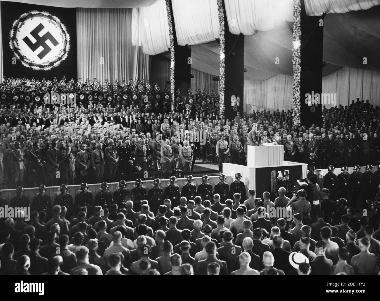 Rudolf Hess gives a speech in the Nuremberg Luitpoldhalle at the opening of the party congress of the NSDAP, here in memory of the late Reich President Paul von Hindenburg. In the 1st row, from right (left side): Julius Streicher, Adolf Hitler (behind him Wilhelm Brueckner), Viktor Lutze, Heinrich Himmler, Franz Xaver Schwarz, Robert Ley, Joseph Goebbels. Right side next to Rudolf Hess: Hermann Goering. Stock Photo