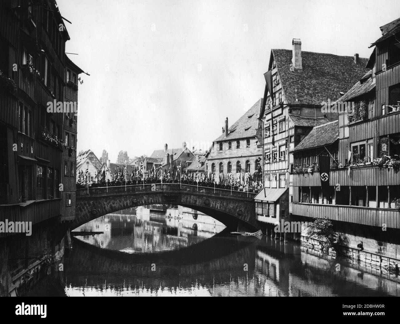 View of the Fleisch Bridge in Nuremberg over the Pegnitz river, on which columns of NSDAP organizations march with swastika flags during the Nazi Party Congress in Nuremberg. Stock Photo