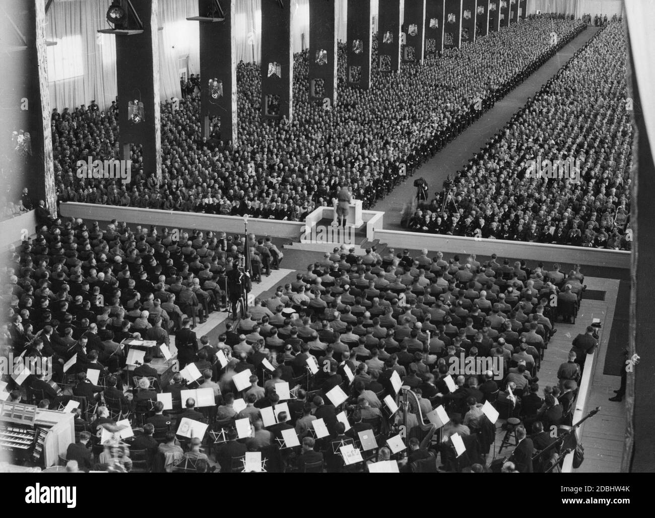 Rudolf Hess gives a speech at the opening of the party congress in Nuremberg's Luitpoldhalle, filmed by a cameraman. In the foreground is a music orchestra. Stock Photo