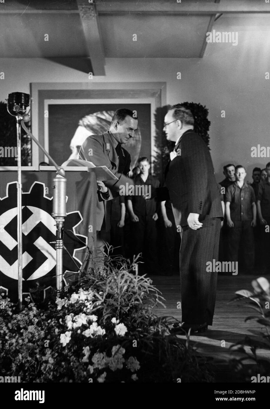 Alfred Spangenberg, Gauobmann (District Leader) of the DAF, presents Director Speck from the Werkzeugfabrik R. Stock & Co. in Berlin-Marienfelde with an award certificate as a DAF achievement badge for the vocational training. In the background there is a larger-than-life portrait of Adolf Hitler and several apprentices. Stock Photo