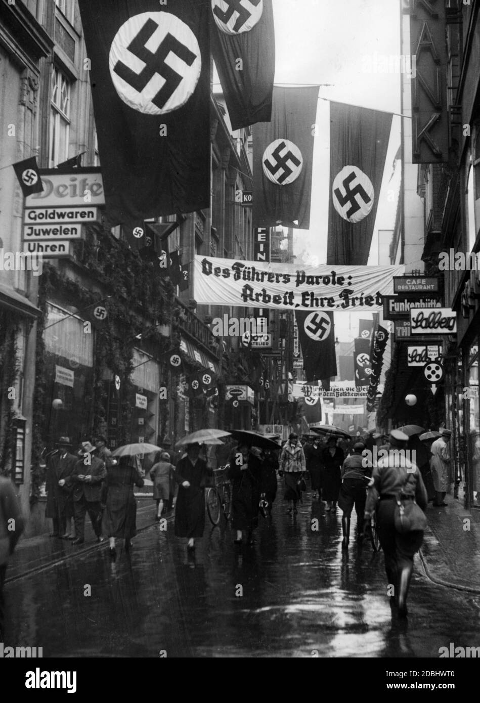 'Street scene in Essen. The street was flagged with swastika flags. In the street there is a banner reading ''The Fuehrer's slogan: Work, Honor, Peace''.' Stock Photo