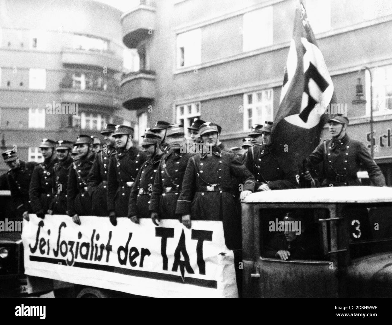 'SA members stand on the loading area of a truck. On the truck is a banner saying ''Sei Sozialist der Tat'' (Be a socialist in action). (undated photo)' Stock Photo